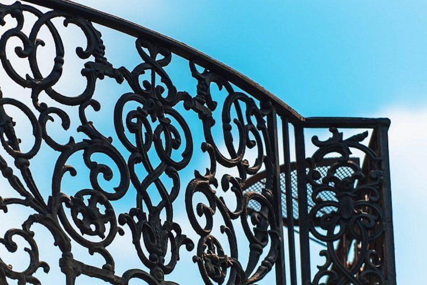 A black wrought iron gate with intricate scrollwork against a clear blue sky. 3