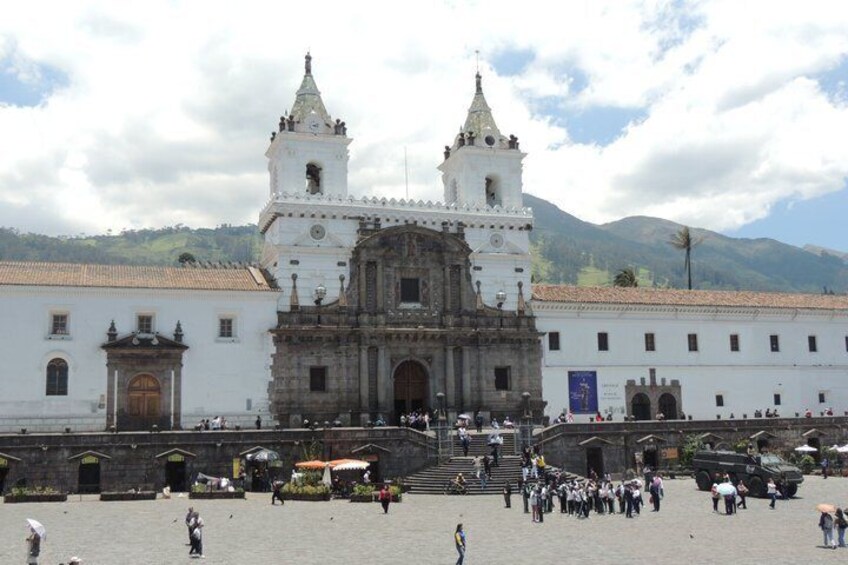 A historic cathedral with two towers, a plaza with people, and mountains in the background. 5