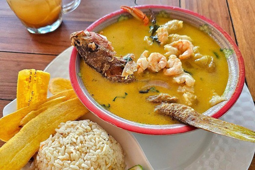 A bowl of soup with shrimp and a fish, accompanied by rice and plantain chips. 3