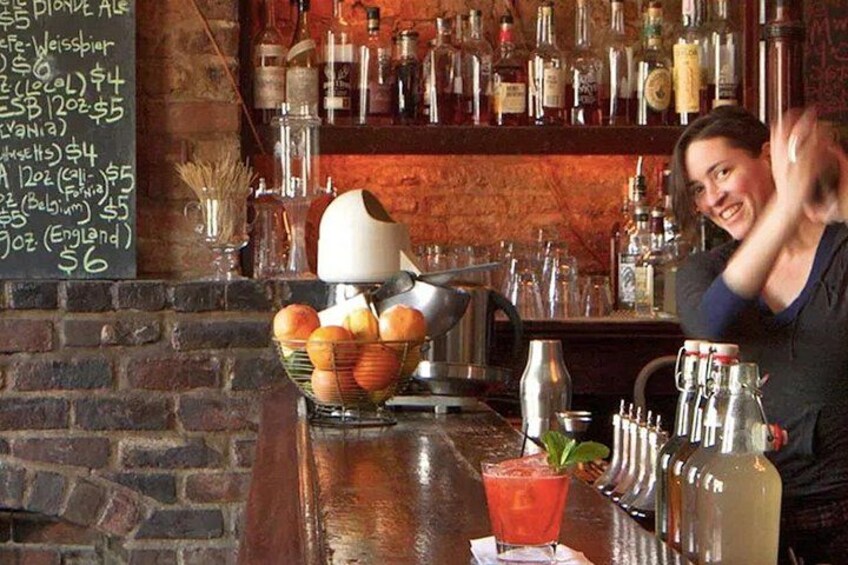 A bar with a brick wall, shelves of bottles, a chalkboard menu, and a bartender. 2