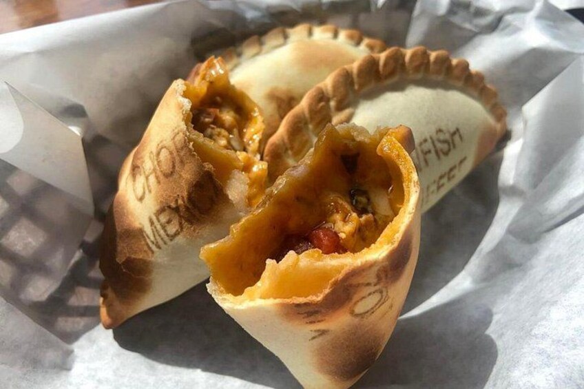 A half-eaten empanada with visible filling and a label reading 'CHOC. MEX.' 5