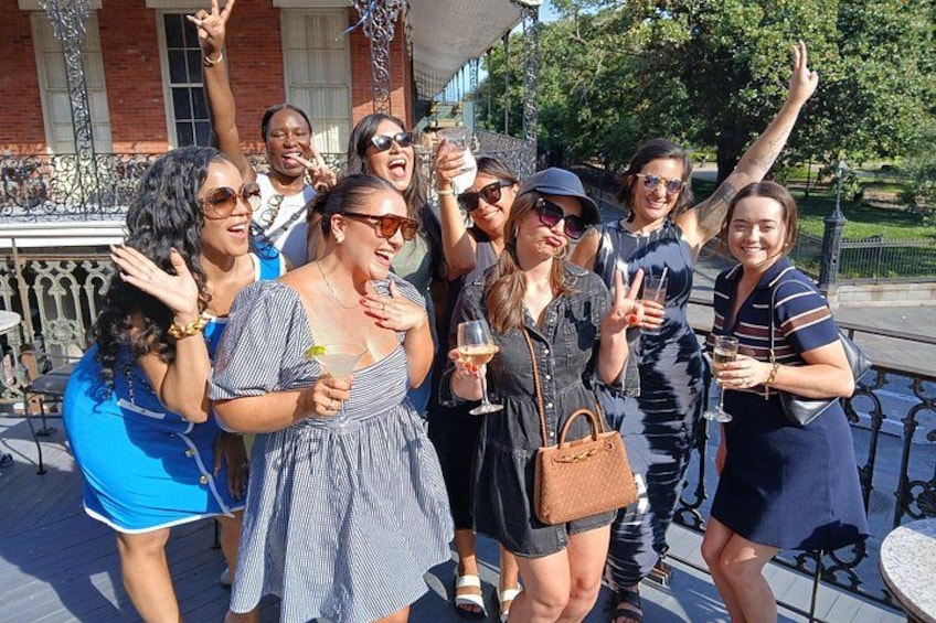 A group of people outdoors, some holding drinks, with a building and trees in the background. 4