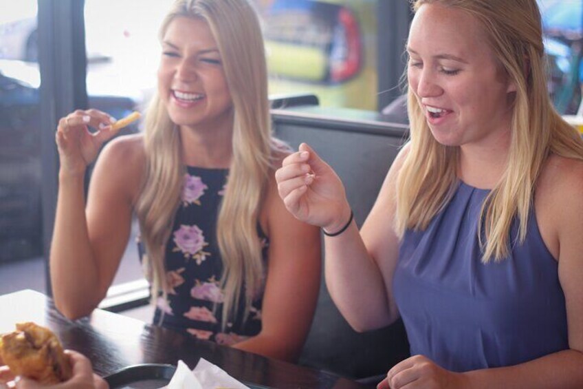 Two people sitting at a table, one eating a fried item. 5