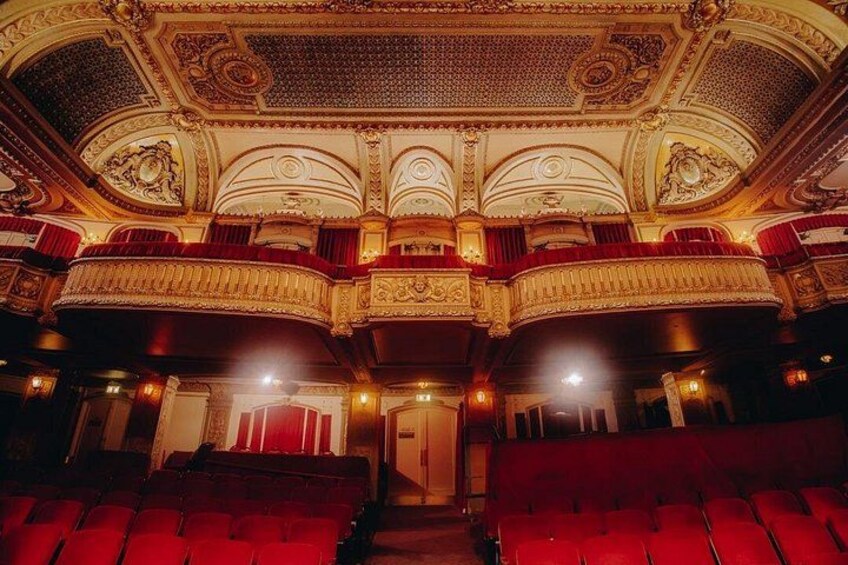 Ein prunkvolles Theaterinneres mit roten Sitzen und aufwändiger Goldverzierung an der Decke. 5