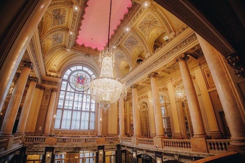 Ein prunkvolles Interieur mit einer großen Chandelieber, Säulen und einer imposanten Treppe. 2