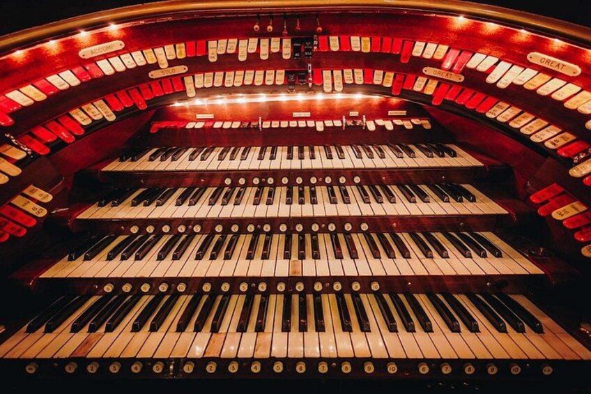 Eine prächtige Orgel mit mehreren Klaviaturen und Pfeifen, beleuchtet durch rotes Licht. 3