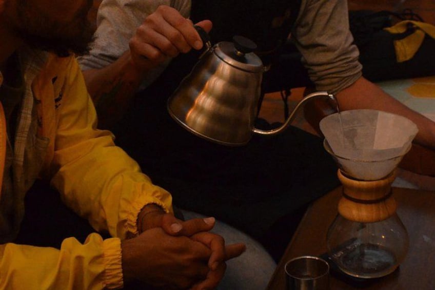 Una persona sosteniendo una tetera de metal, una taza de vidrio y un objeto de madera sobre una mesa. 4