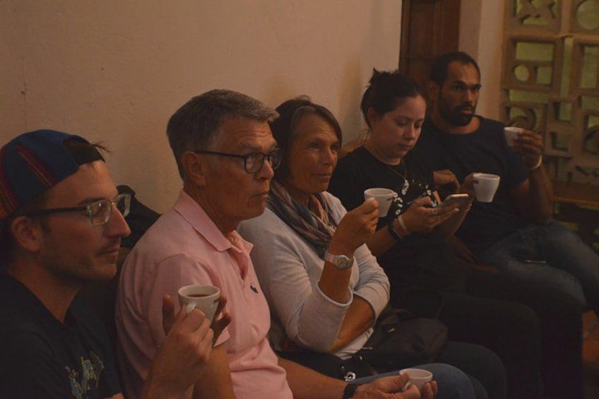 Un grupo de personas sentadas en sillas, sosteniendo tazas, presumiblemente en un ambiente interior informal. 2