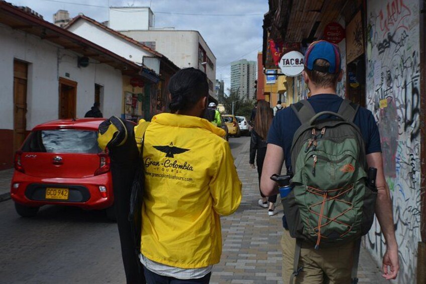 Una calle con un coche rojo, paredes con grafitis y gente caminando. 5