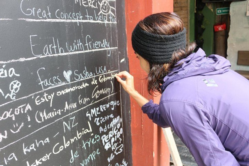A person writing on a blackboard with chalk, wearing a purple jacket. 2