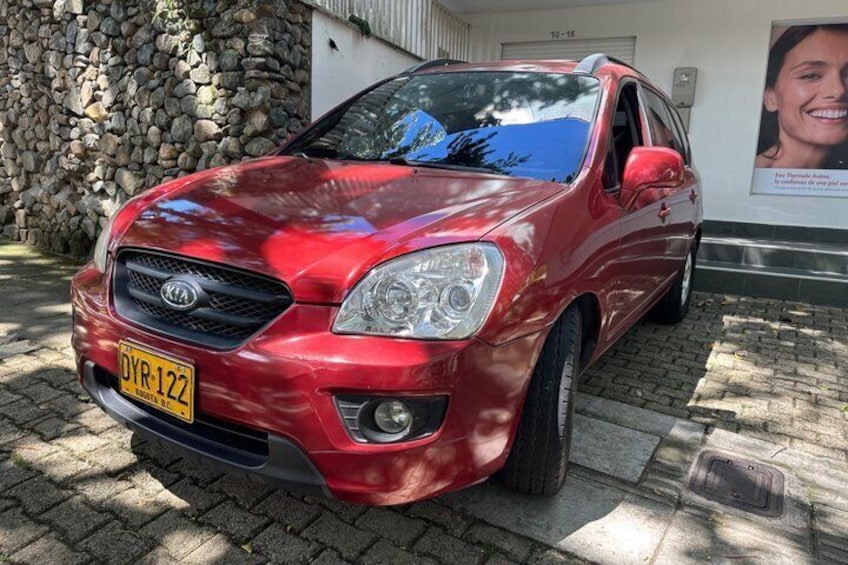 Un coche Kia rojo aparcado en un camino empedrado, con un muro de piedra y un edificio al fondo. 5