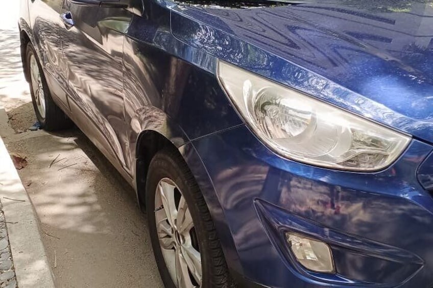 Un coche azul estacionado en una calle con aceras y árboles al fondo. 2