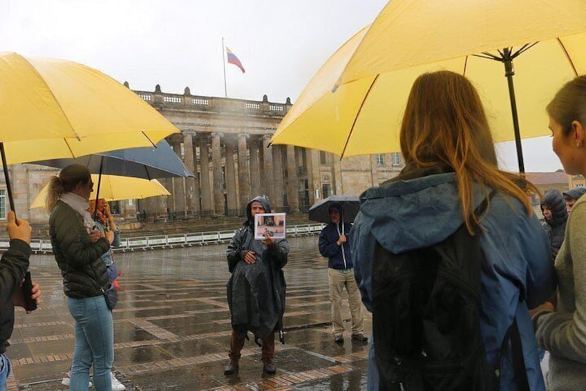 A group of people holding umbrellas, standing in front of a large building with columns and a flag. 4