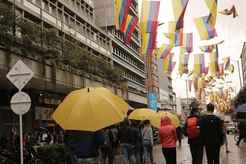 A street with people walking under yellow umbrellas, buildings with vines, and flags hanging overhead. 5