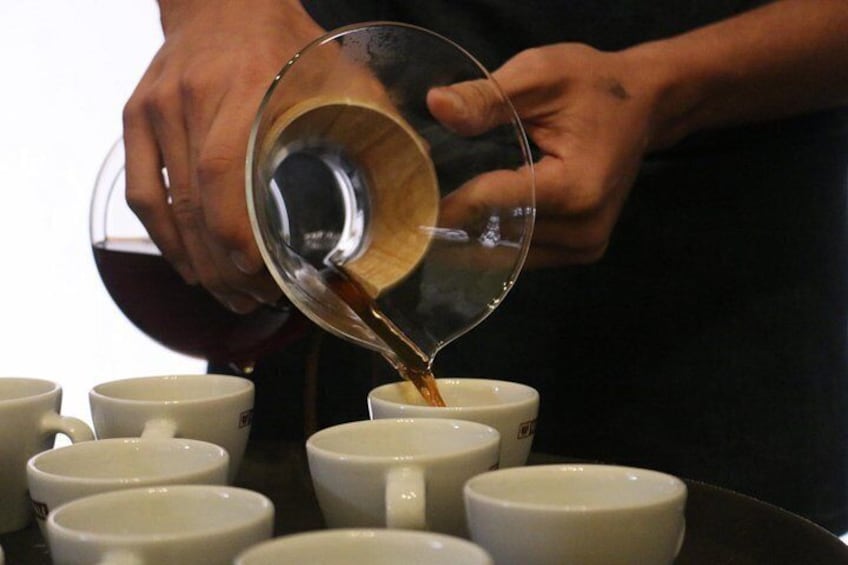 A person pouring liquid from a glass into a white mug. 2