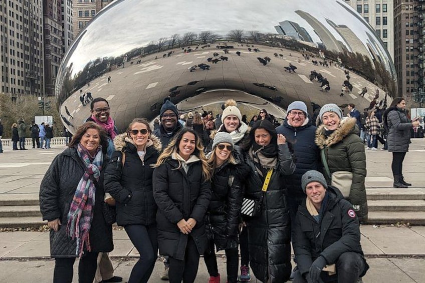 A group of people posing in front of a large metallic sculpture with a reflective surface. 1
