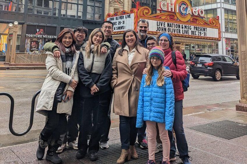 A group of people posing in front of a theater with a sign advertising a live show. 5