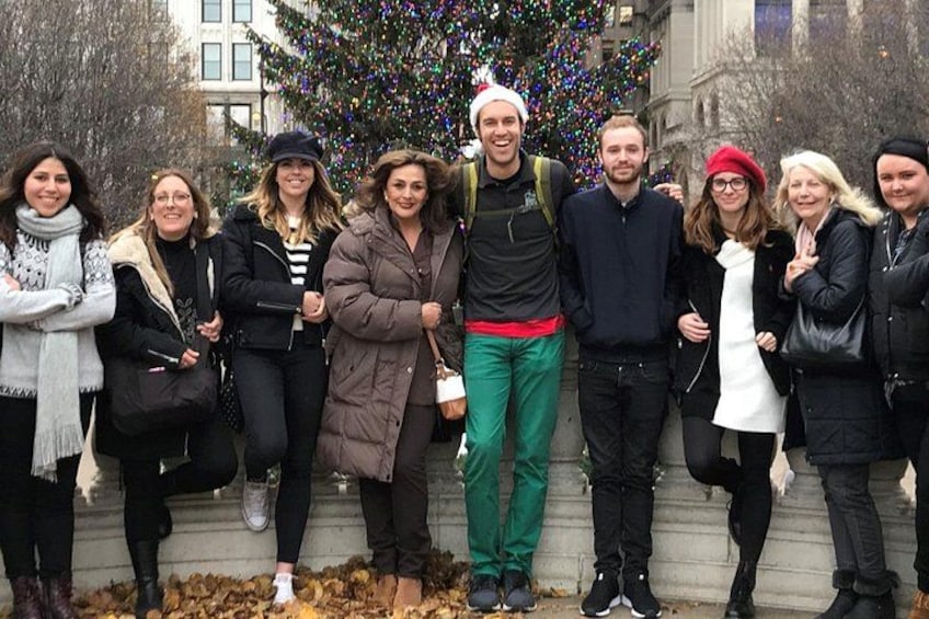 A group of people standing in front of a building with a Christmas tree. 3