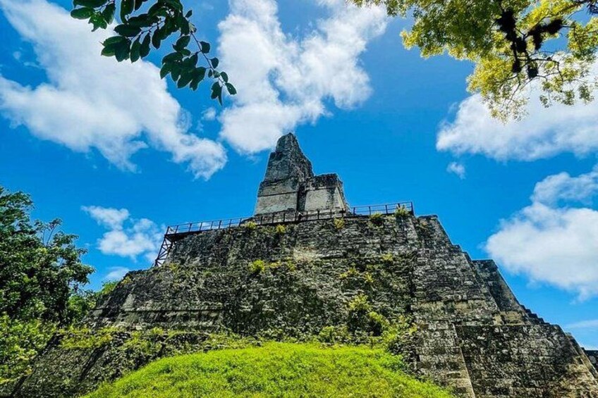 Een enorme, oude piramide met een platte bovenkant, omringd door groen en onder een heldere blauwe lucht. 2