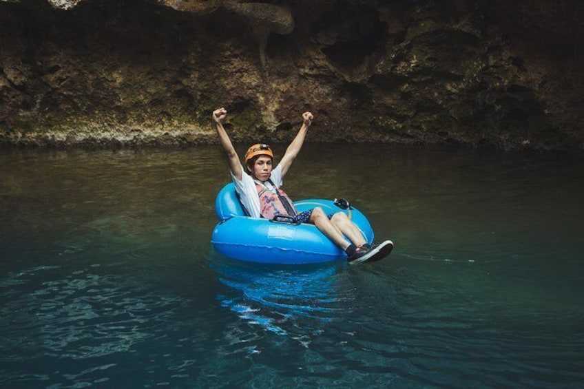 A person floating on a blue inflatable raft in clear water with a rocky background. 1