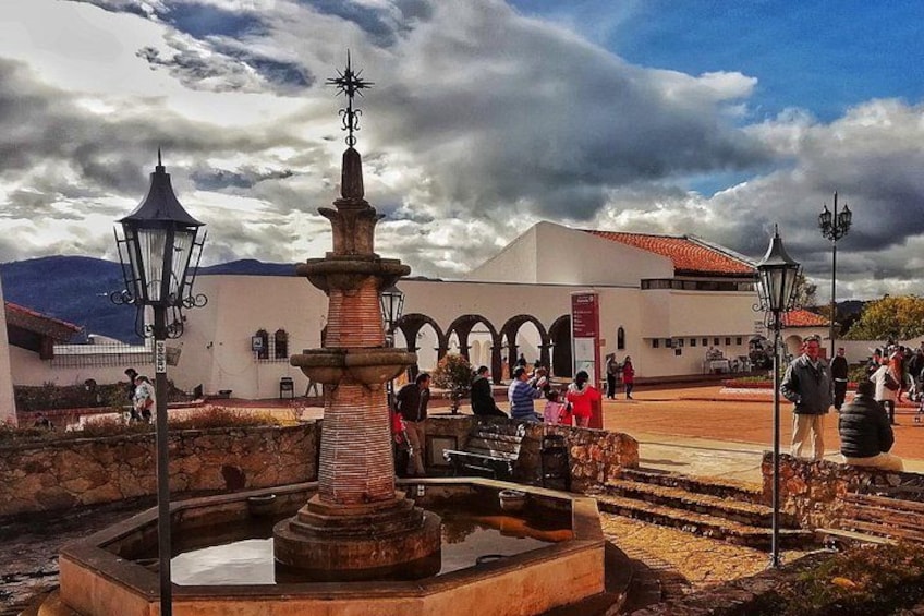 Ein Brunnen, ein weißes Gebäude mit Bögen und ein bewölkter Himmel. 4