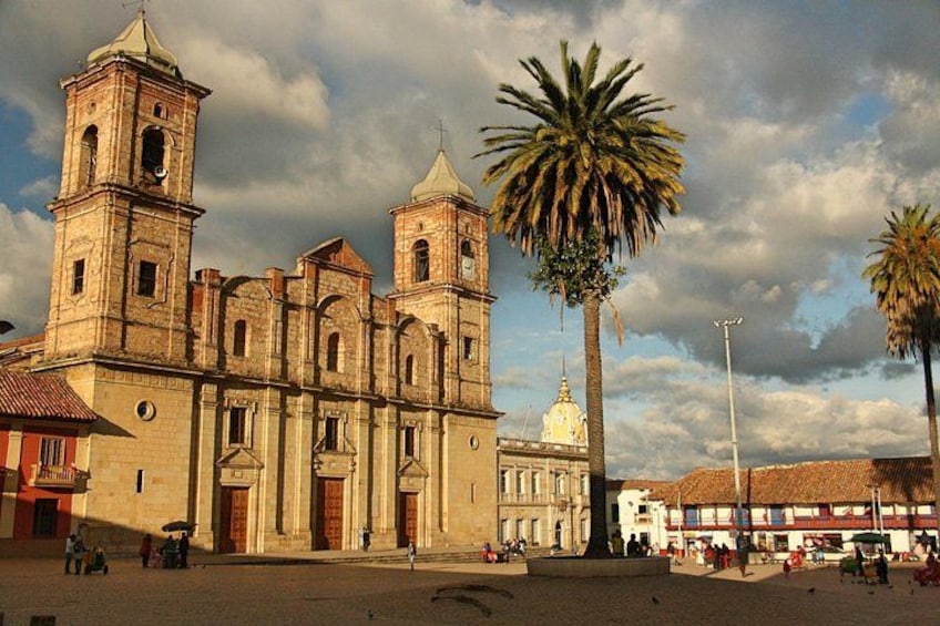 A historic church with two bell towers, palm trees, and a plaza with people. 2