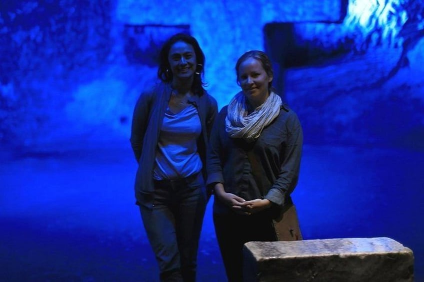 Two people standing in a dimly lit room with a stone block on the floor. 1