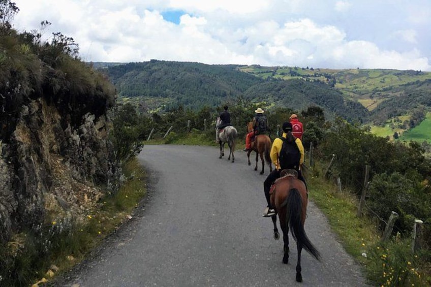 A group of people riding horses on a narrow road surrounded by hills and greenery. 2