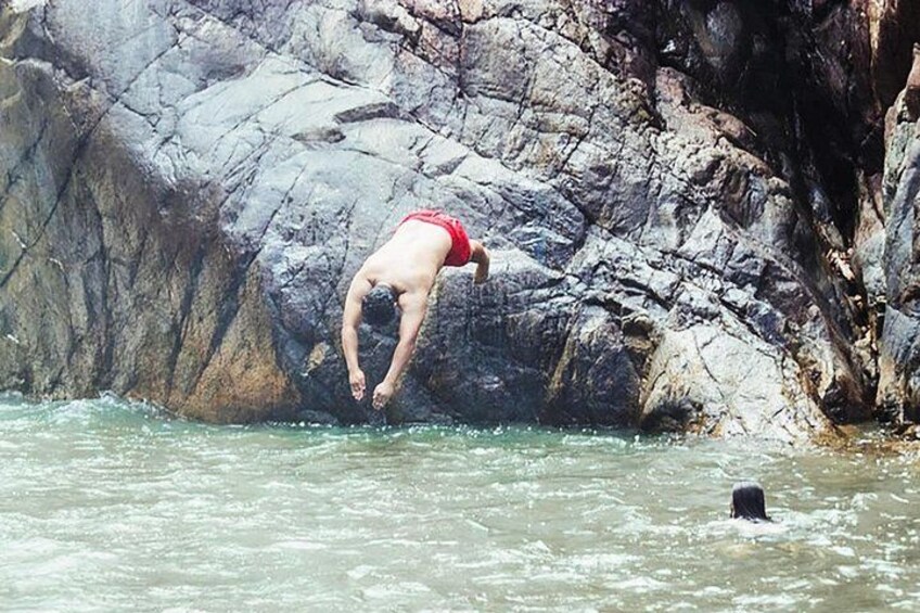 En person i röda badshorts som dyker från en klippig klippa ner i vattnet. 3