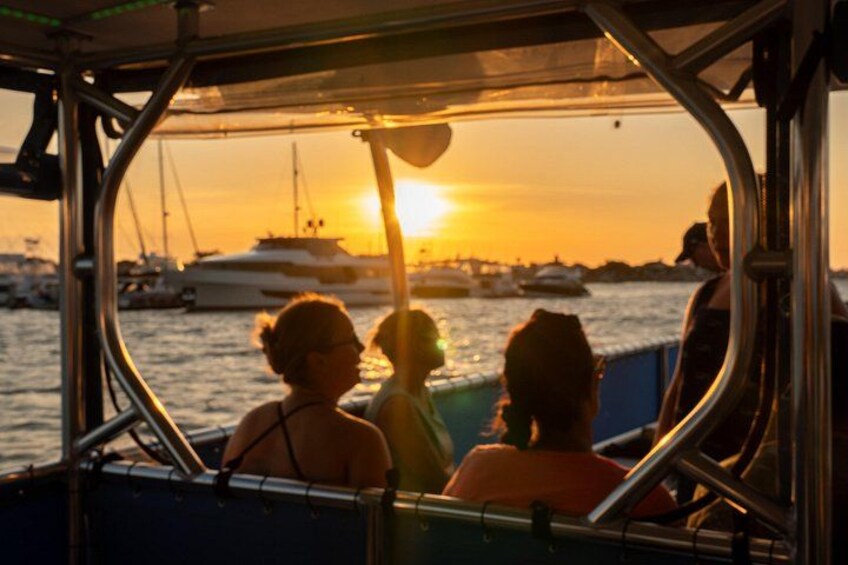 Un barco con gente a bordo, una puesta de sol y varios barcos al fondo. 2