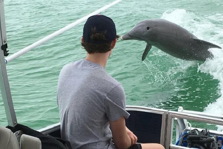 A person on a boat with a dolphin jumping out of the water. 4