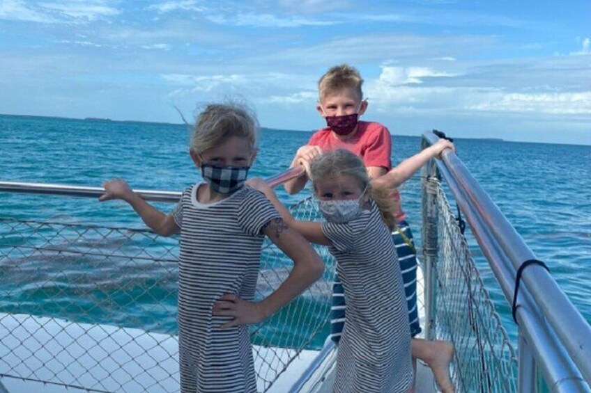 Two children on a boat deck, one wearing a striped dress and the other in a red shirt, with the ocean and a ship in the background. 5