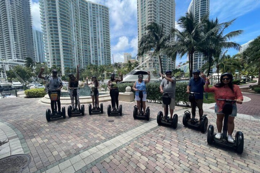En gruppe mennesker på segways på en belagt flade med palmer og høje bygninger i baggrunden. 2