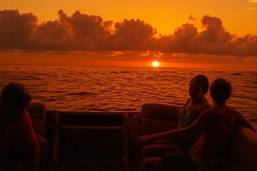 A sunset over the ocean with a boat and people on the deck. 2