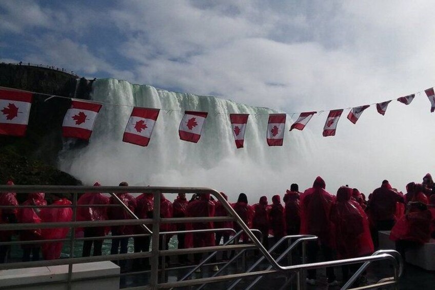 Un gruppo di persone con giacche rosse che osserva una cascata, con presenti bandiere canadesi. 3