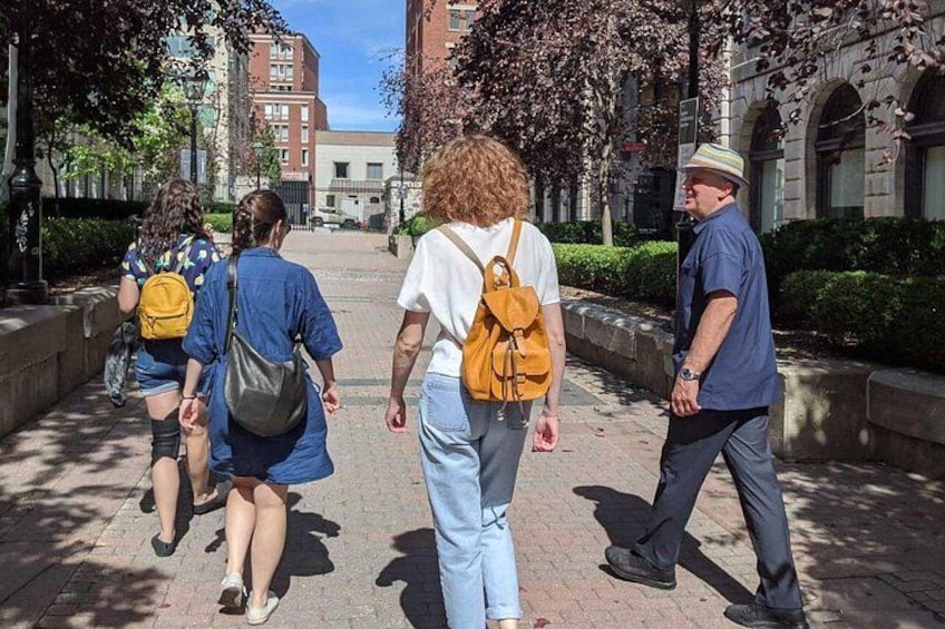 Un gruppo di persone cammina su un sentiero lastricato, con alberi ed edifici sullo sfondo. 3
