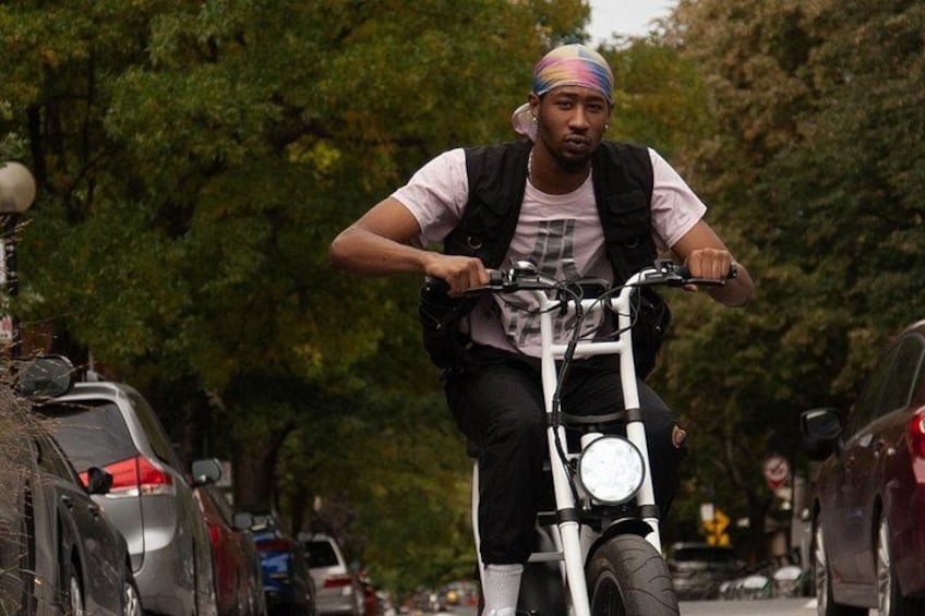 A person riding a bicycle on a tree-lined street with parked cars. 3