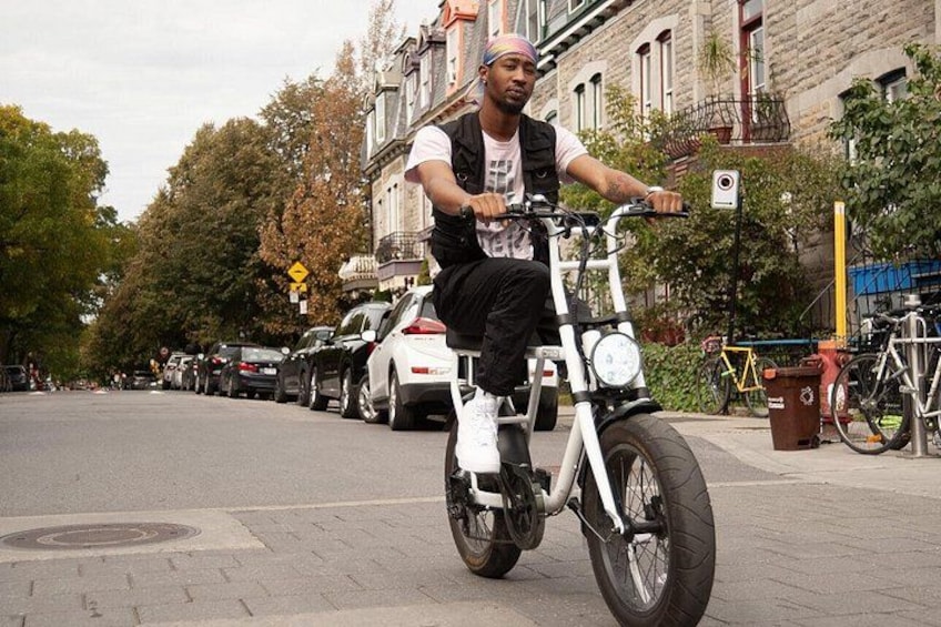 A person riding a white bicycle on a city street with parked cars and bicycles. 4