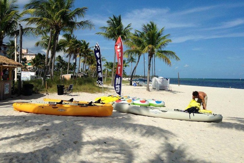 Une plage avec des kayaks, un drapeau de surveillance et des palmiers. 3