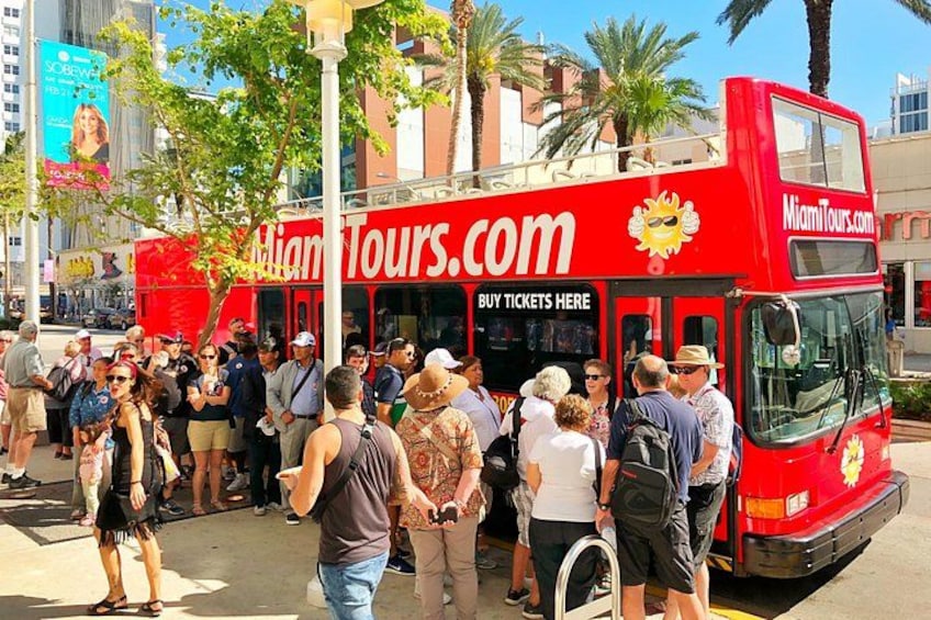 A red double-decker bus with 'MiamiTours.com' written on it, surrounded by a crowd of people. 1
