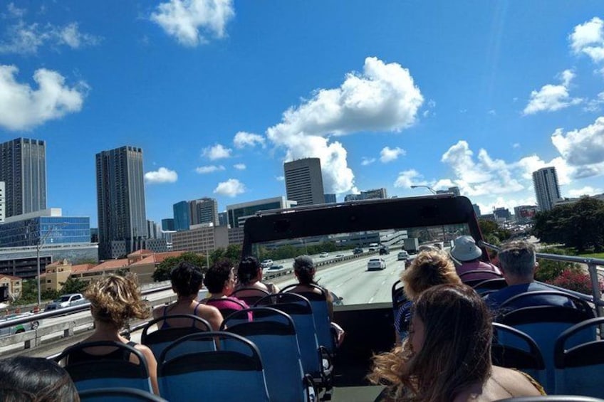 Un groupe de personnes participe à une visite guidée en autobus et observe un paysage urbain caractérisé par de hauts immeubles et un ciel dégagé. 5