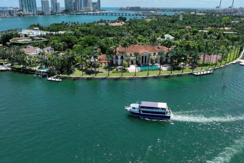 A boat on a turquoise body of water, surrounded by lush greenery and a large house with a red roof. 3