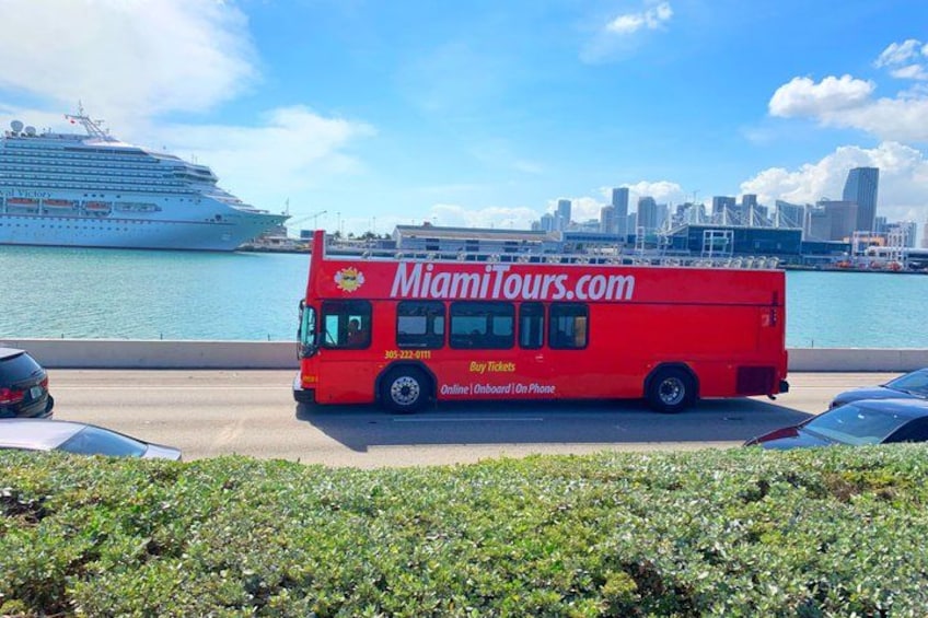Un autobus rouge de MiamiTours.com est garé au bord de l’eau, avec un navire de croisière en arrière-plan. 1