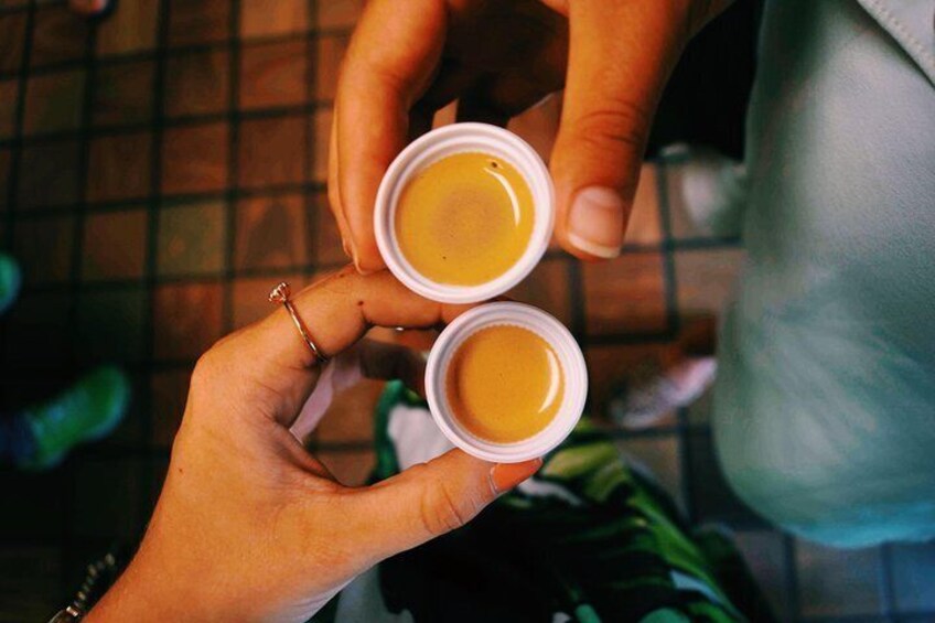 Due mani che tengono piccole tazze bianche con un liquido giallo, probabilmente caffè o tè. 1