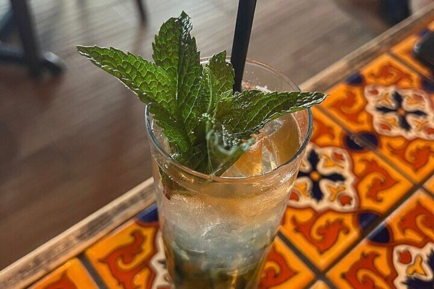 Un bicchiere di bevanda fredda con foglie di menta e una cannuccia su un tavolo con un vivace motivo a mosaico. 2