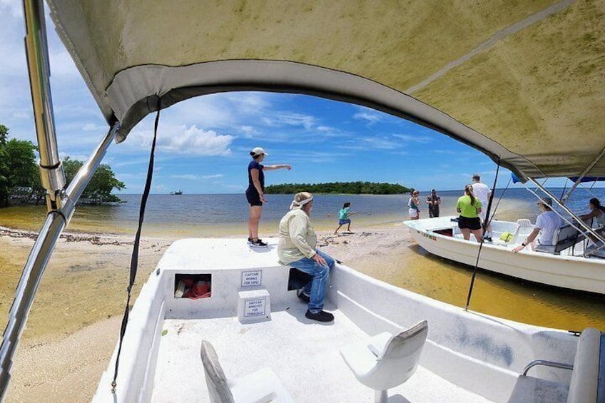 A boat on a sandy shore with people on the beach and in the water. 5