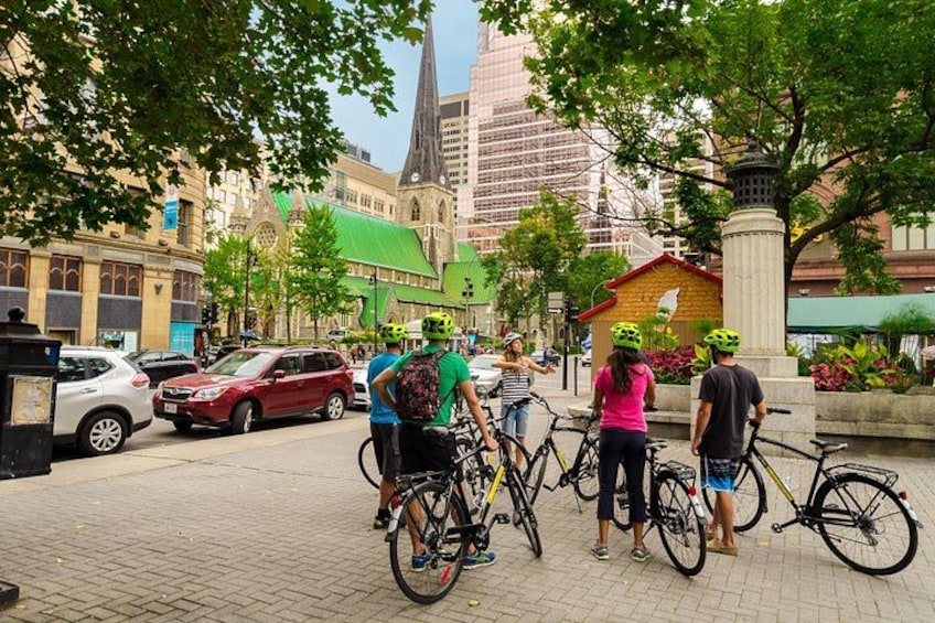 A group of people with bicycles in an urban setting with buildings and a church in the background. 1
