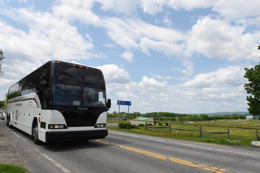 A large white bus on a multi-lane road with a grassy area and a blue sky with clouds in the background. 3