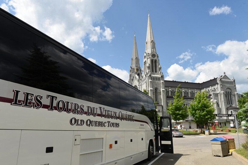 A white bus with 'LES TOURS DU VIEUX QUÉBEC' written on it, parked in front of a cathedral with two spires. 2