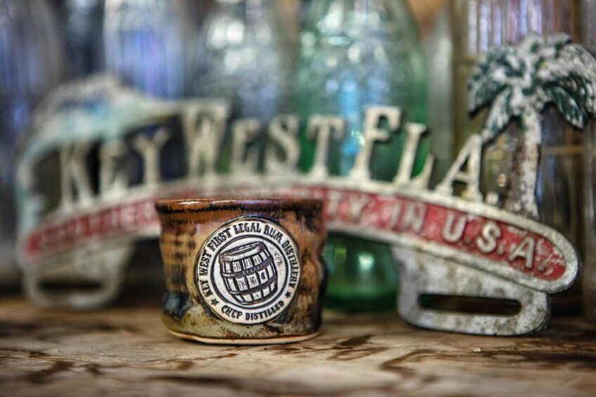 A rustic metal cup with a logo, surrounded by vintage glass bottles and a metal sign with 'KEY WEST U.S.A.' 4